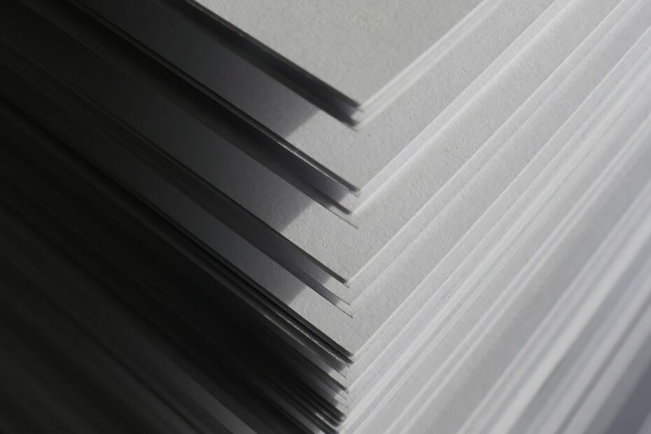 Artistic close-up of stacked white paper sheets creating geometric shadows and patterns in soft light.
